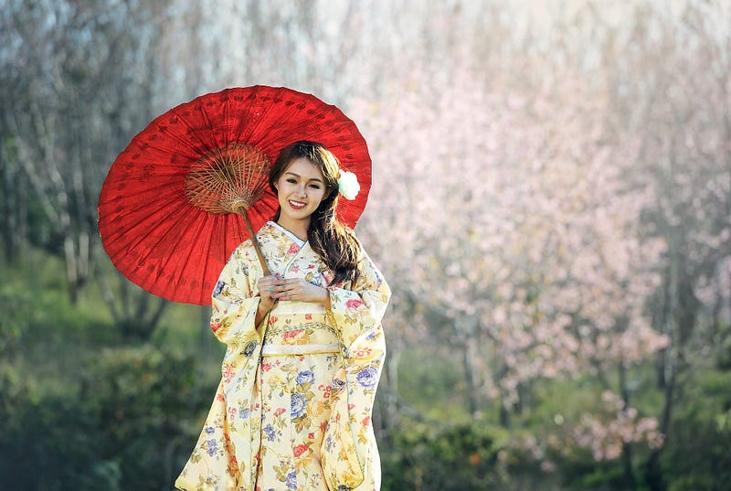 Beautiful Japanese woman in yellow kimono holding a bamboo umbrella in a forest.