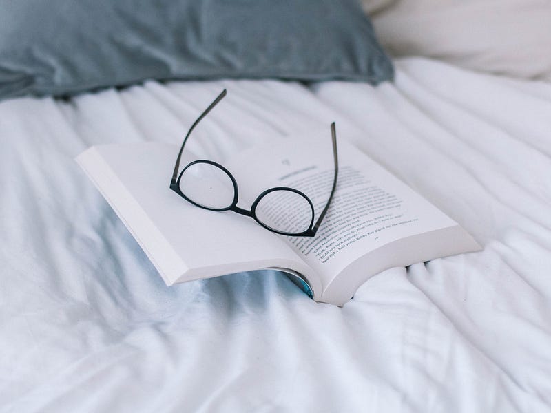 A book with glasses on it sitting on a bed.
