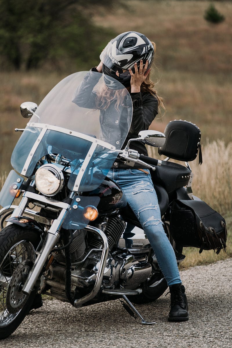 Woman on motorcycle removing helmet.