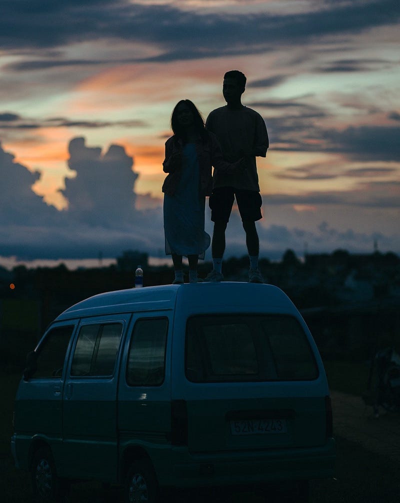 Couple watching the sunset on top of van.